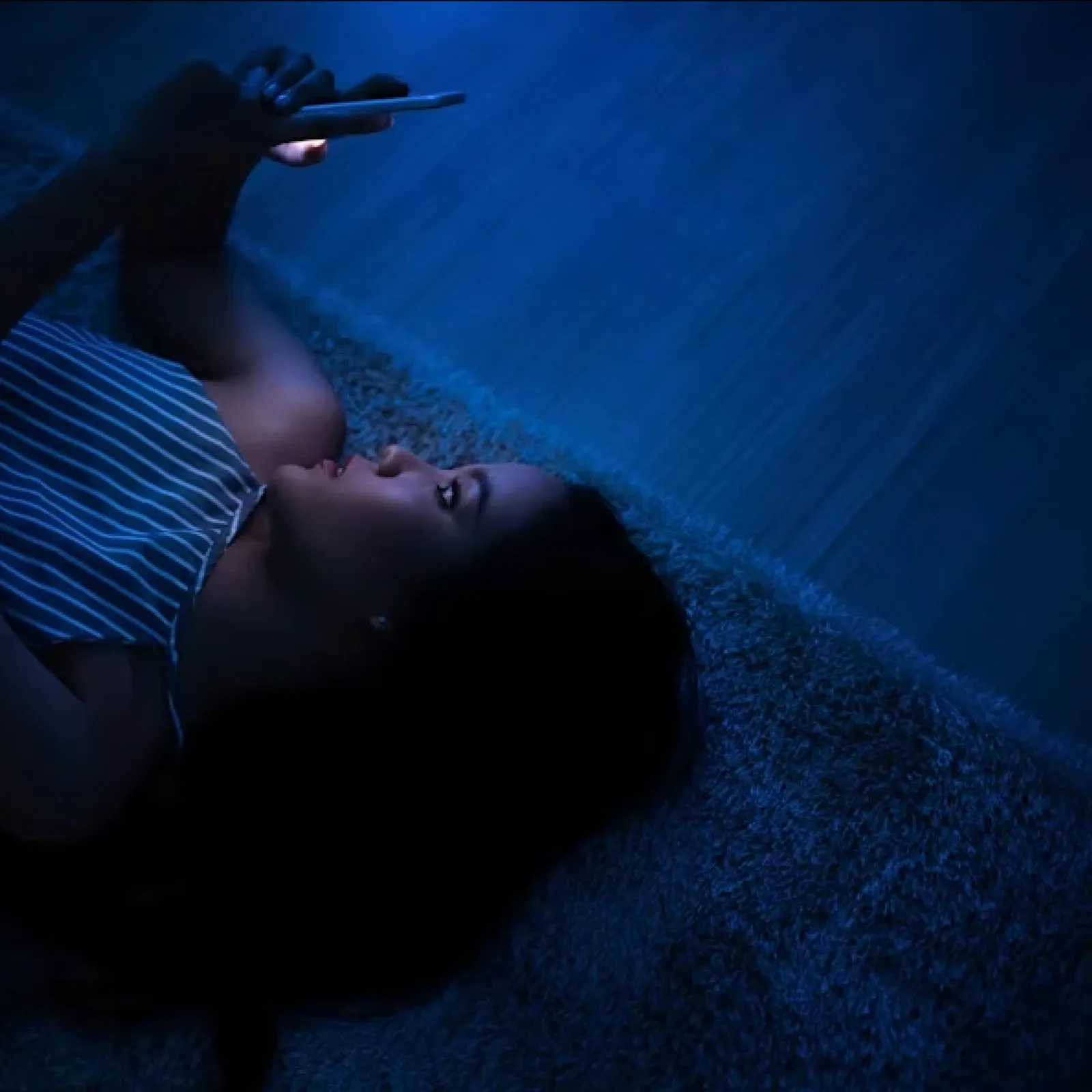 A woman lying in bed lit by the blue glow of her phone